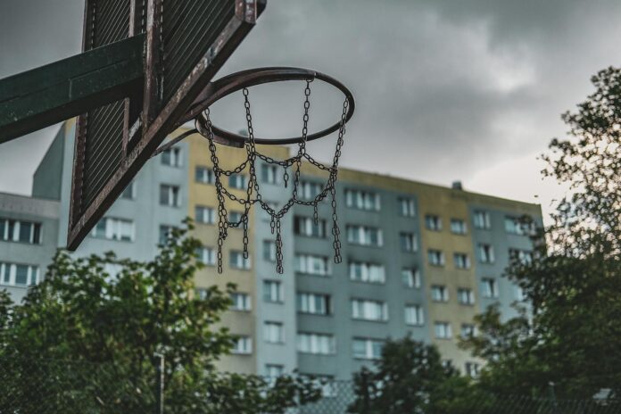Rusty basketball hoop in a Gdańsk neighborhood with residential buildings on a cloudy day.