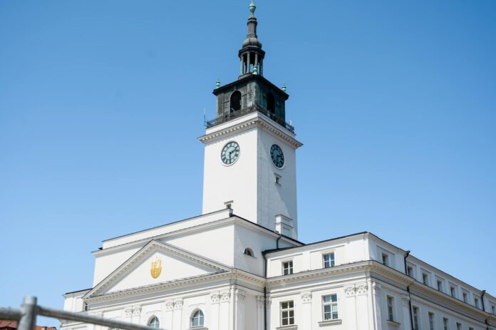 Elegant white facade of the historic Kalisz Town Hall with a clock tower against a blue sky.