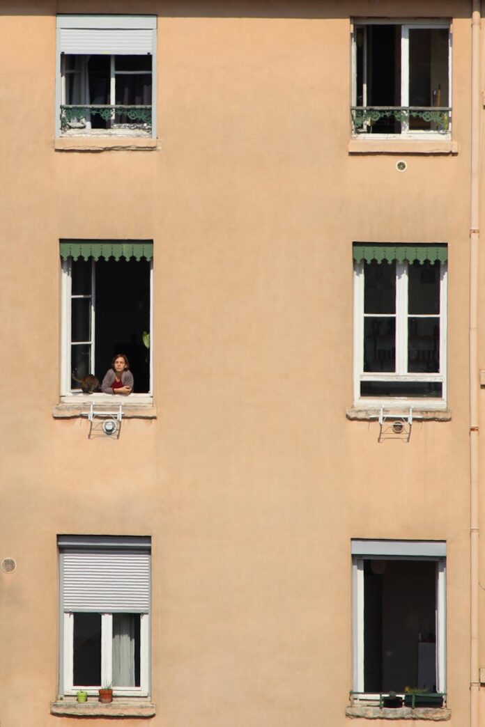 Person looking out from an apartment window in Lyon, France, highlighting themes of isolation and urban living.