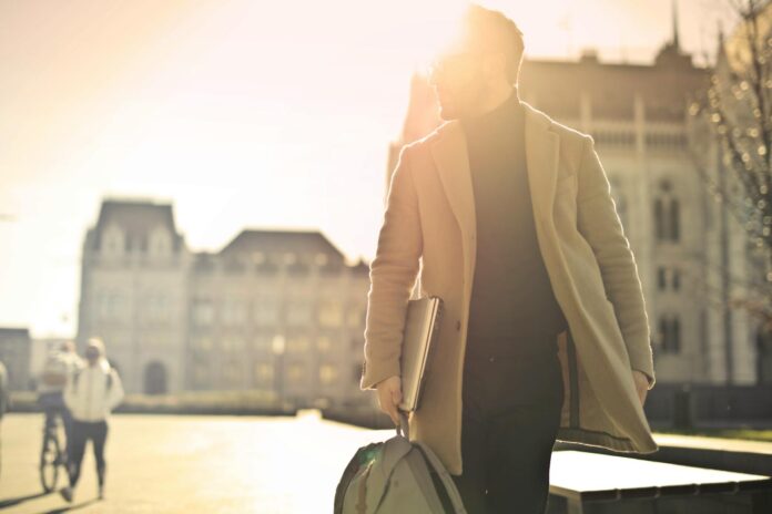 A businessman walks in front of a historic building in Budapest with sun glare illuminating the scene.